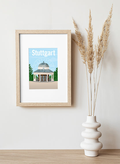 A frame with a postcard of the Stuttgart Teehaus, hung on a white wall, above a wooden shelf, on which is a white ceramic vase containing reeds.