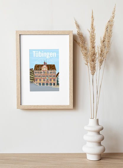 A frame with a postcard of the Tübingen Rathaus, hung on a white wall, above a wooden shelf, on which is a white ceramic vase containing reeds.