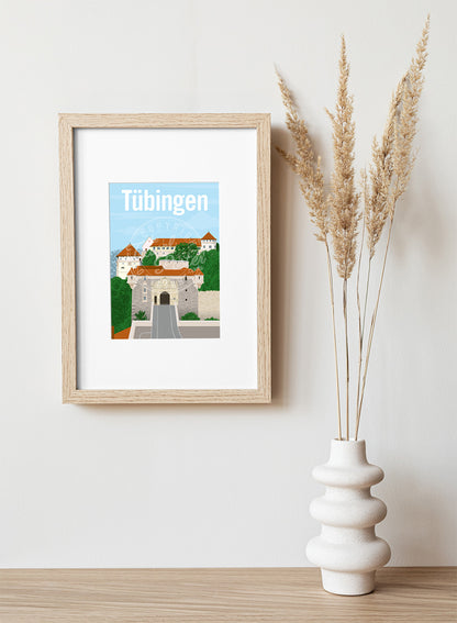 a frame with a postcard of Tübingen Castle, hung on a white wall, above a wooden shelf, on which is a white ceramic vase containing reeds.